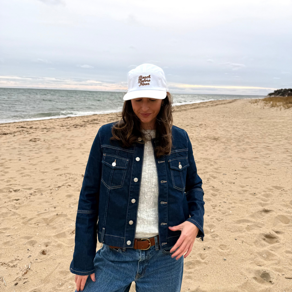 Person wearing a denim jacket and white cap on a beach